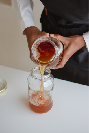  glass of freshly brewed homemade kombucha with a SCOBY floating on top, surrounded by ingredients like tea and sugar, representing the fermentation process.

