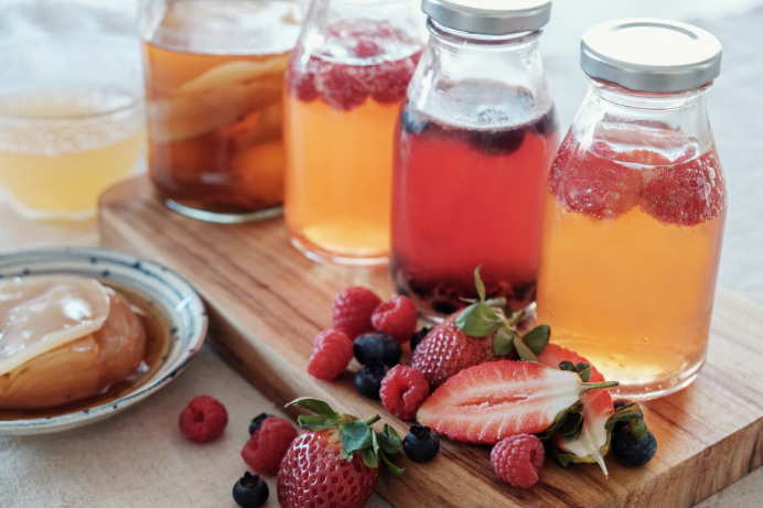 A glass of freshly brewed homemade kombucha with a SCOBY floating on top, surrounded by ingredients like tea and sugar, representing the fermentation process.