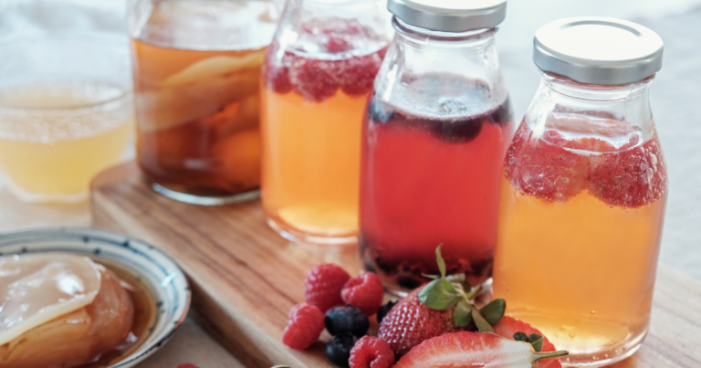 A glass of freshly brewed homemade kombucha with a SCOBY floating on top, surrounded by ingredients like tea and sugar, representing the fermentation process.
